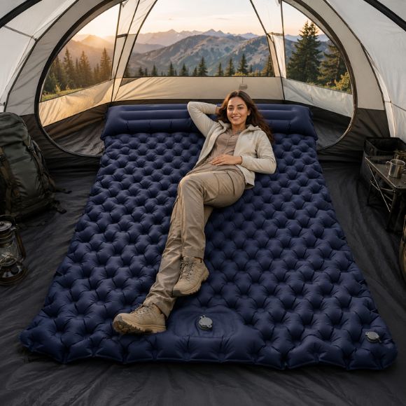Matelas gonflable 2 personnes avec oreillers intégrés, installé dans une grande tente de camping, avec une femme souriante en tenue de randonnée profitant d’un couchage confortable en pleine nature montagneuse.