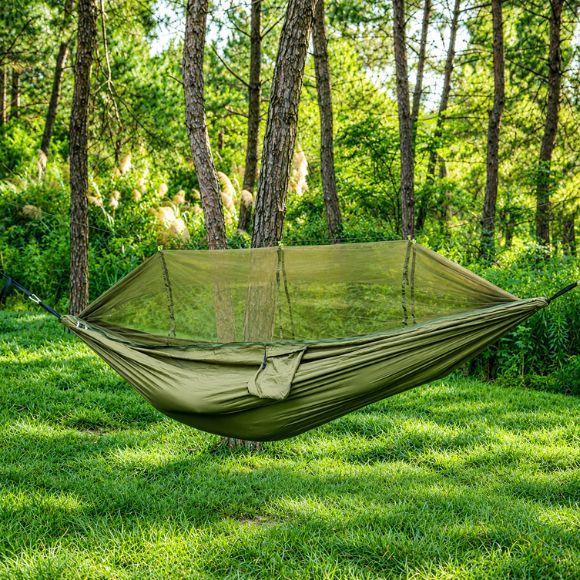 Hamac moustiquaire Hamac suspendue avec moustiquaire vert kaki installé entre deux arbres dans une clairière, idéal pour le camping et le bivouac.