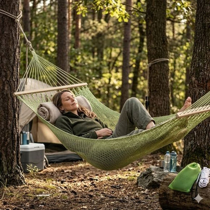 Hamac suspendu en toile verte tressée installé entre deux arbres avec une personne qui se repose en forêt.