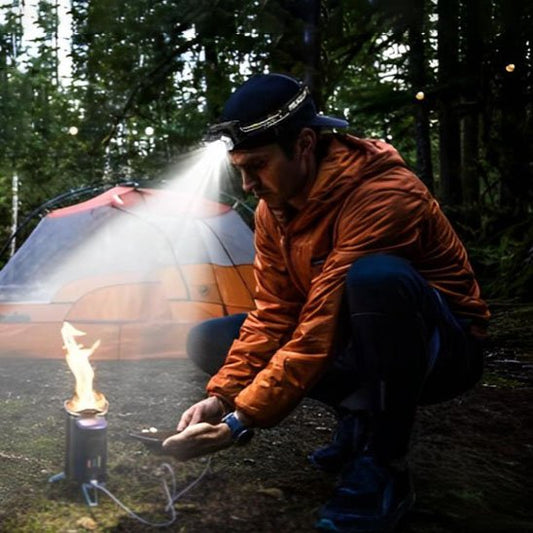 Lampe frontale rechargeable éclairant un campeur près du feu