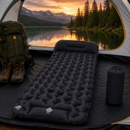 Matelas gonflable de camping noir avec oreiller intégré installé dans une tente face à un lac de montagne au coucher du soleil.