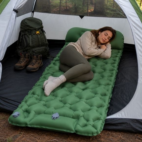 Matelas gonflable TrekRest vert avec oreiller intégré dans une tente de camping, où une femme dort paisiblement, illustrant le confort du couchage pour la randonnée, le bivouac et les nuits en pleine nature.